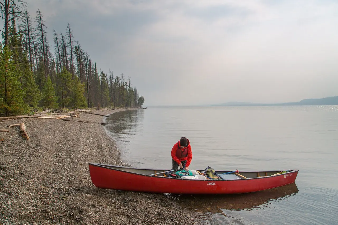 A person loading a canoe on the shore of a lake. » Outdoors International A person loading a canoe on the shore of a lake.
