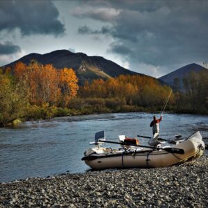 Inflatable boat tied to a rocky riverbank with autumn trees and mountains under a cloudy sky