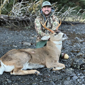 img-2496-copy-jpg-x4bfccd-1 » Outdoors International Hunter kneeling on a rocky shoreline beside a deer with brown fur and antlers, posing after a hunt in camo gear and a green cap.