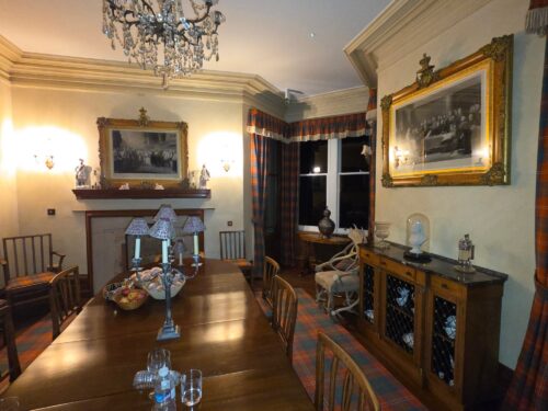 Elegant dining room with a long wooden table, crystal chandelier, and gilded mirrors on the walls.