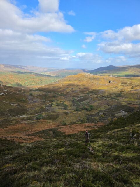 Hiker with backpack walking through rolling moorland under a blue sky with scattered clouds.